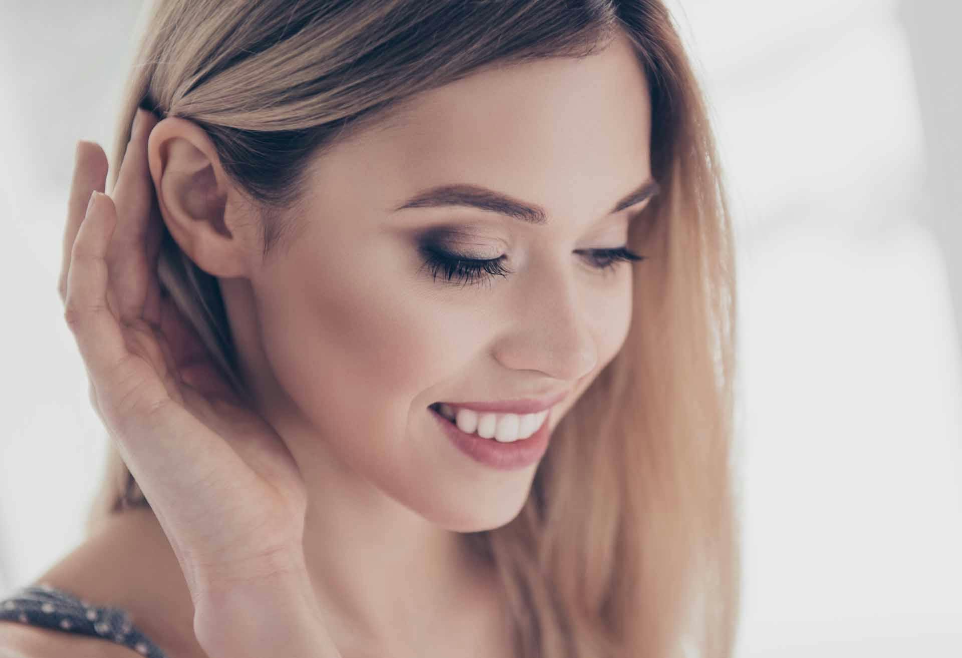 Woman with a hand behind her ear, looking down