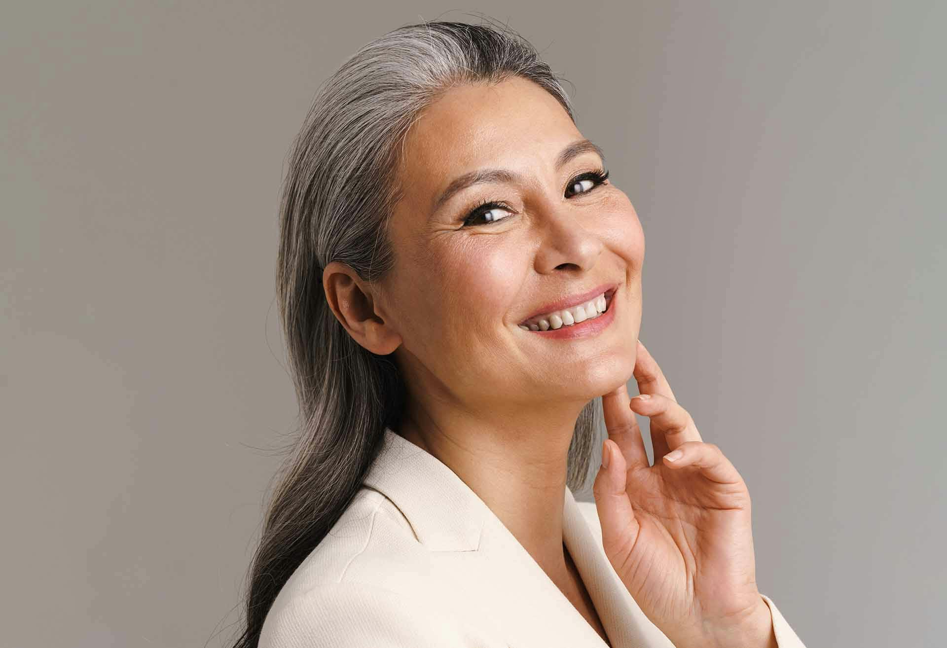 Older woman with gray hair and a hand against her face, smiling