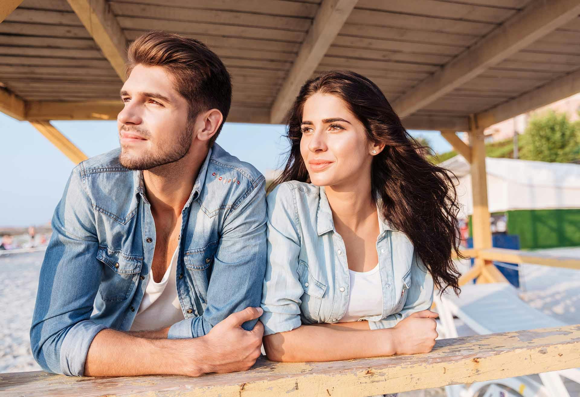 Man and woman resting against a railing at the beach