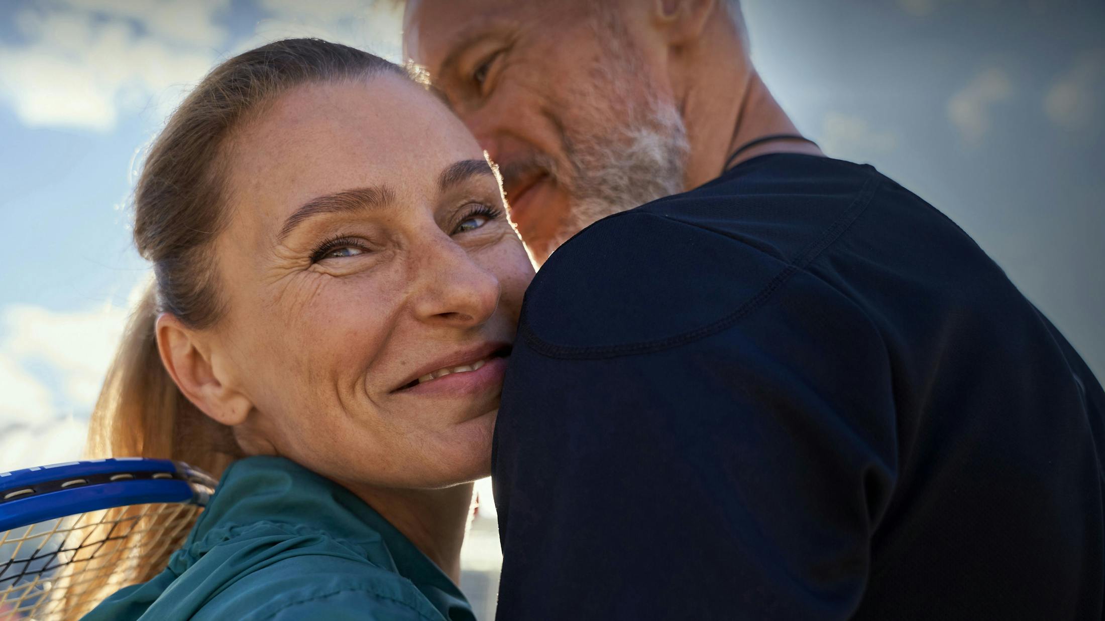 Woman and man hugging while holding tennis rackets.