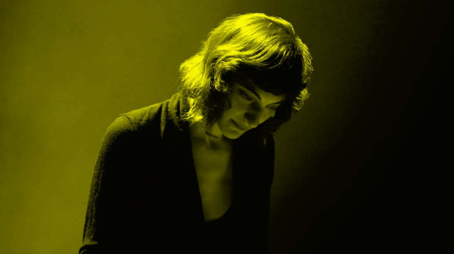 A person with shoulder-length brown hair and light skin looks down.