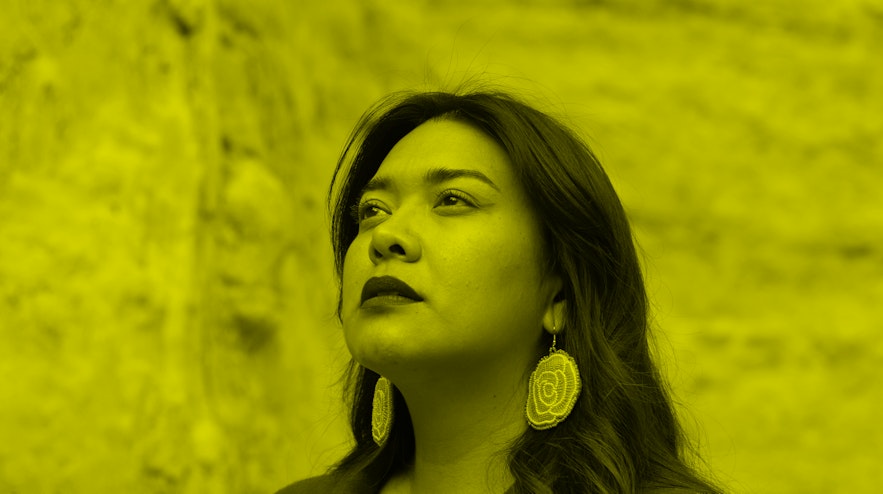A person with long, black hair and light brown skin and looks up into the distance.