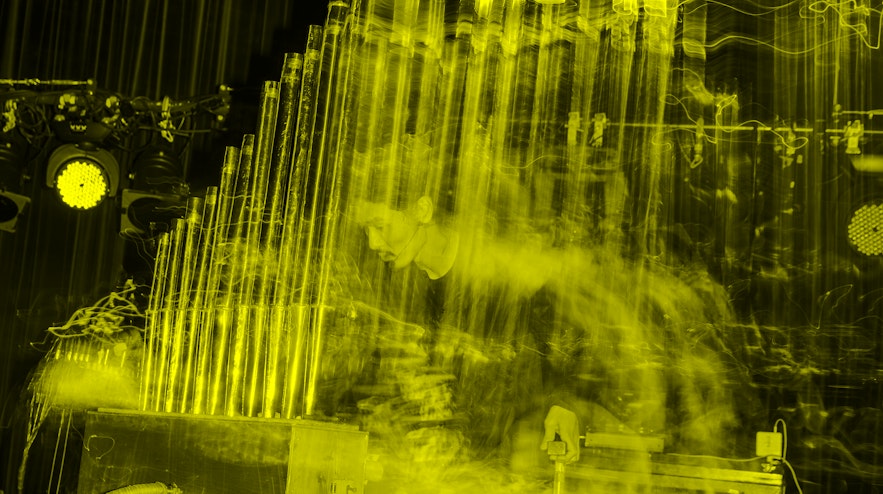 A long-exposure of a person with long black hair and light skin playing a pipe organ.