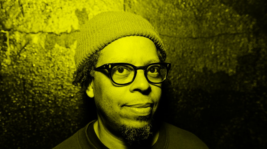 A person with short, black hair and goatee, thick-rimmed glasses and medium brown skin. They are smiling gently.