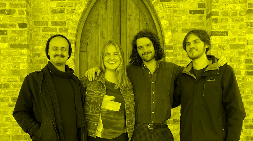 Four people smiling and standing shoulder-to-shoulder in front of a wooden church door.
