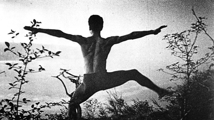 A person viewed from behind with their arms outstretched and legs spread wide, with one leg lifted into the air.