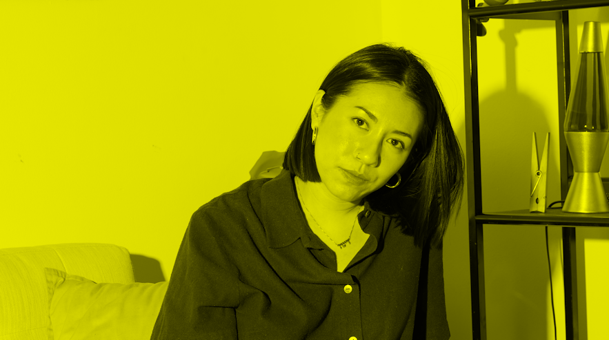 A person with long black hair and light skin sitting on a couch.