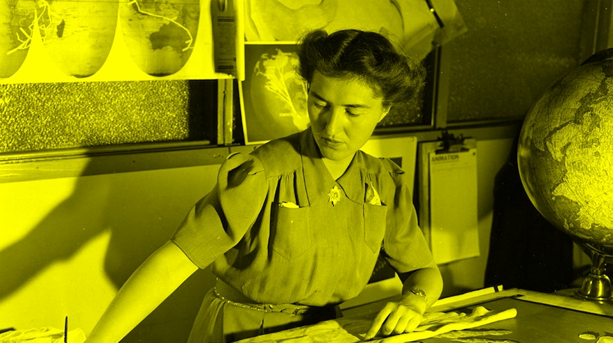 A person with pinned up dark hair and light skin seated at a desk painting a world map.