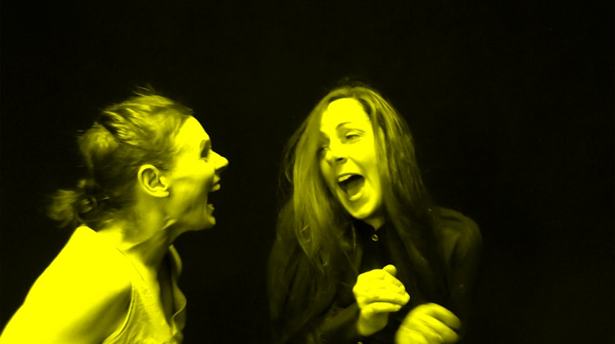 Two people standing next to each other laughing. The person on the left has reddish-brown hair and light skin, the person on the right has crimson and black ahri and light skin.