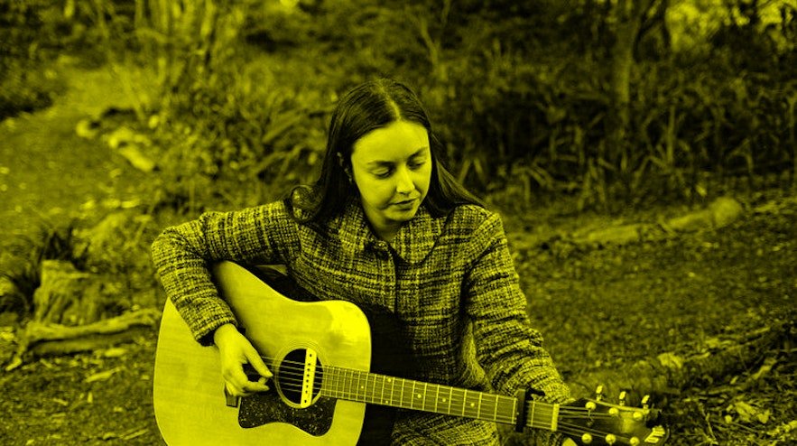 Person sitting in the woods, playing an acoustic guitar.