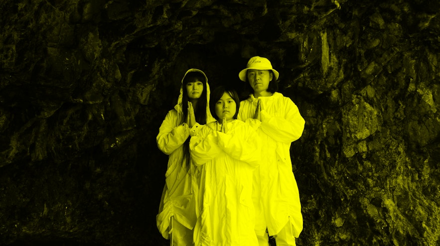 A family of two adults and a young person standing in a cave. All three have their hands clasped together in front of their chests.