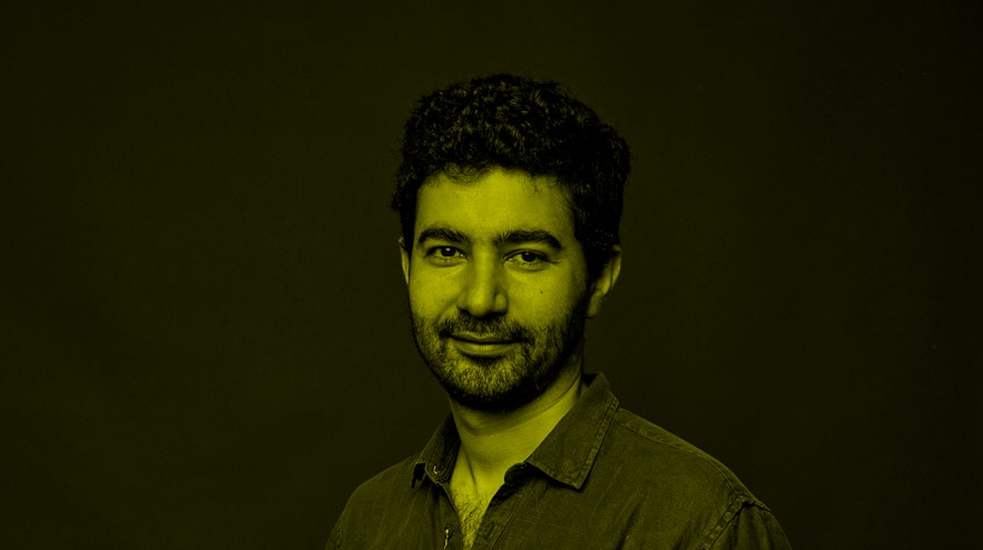 A person with medium brown skin, short black hair and a beard smiling into the camera.