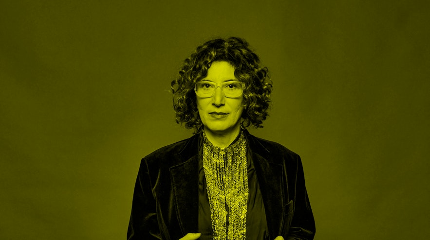A perosn with light skin and curly, dark red hair holding the lapels of their coat.
