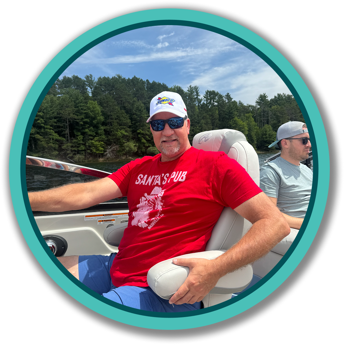 Man in red shirt on a boat with green tree and clear sky