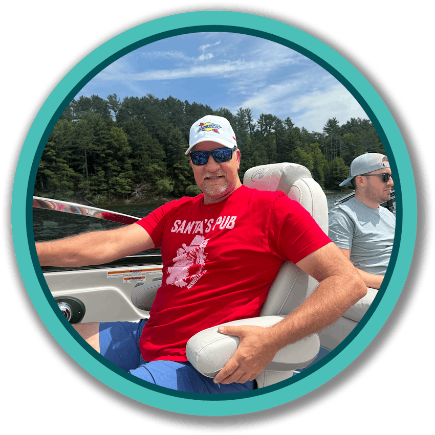 Man in red shirt on a boat with green tree and clear sky