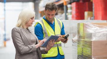 manager using tablet while worker scanning package in warehouse