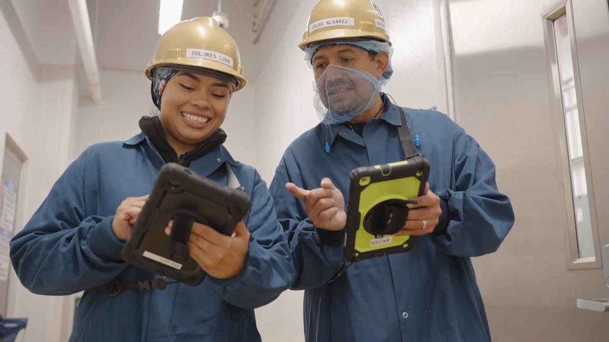 Two food plant workers wearing hard hats holding tablets