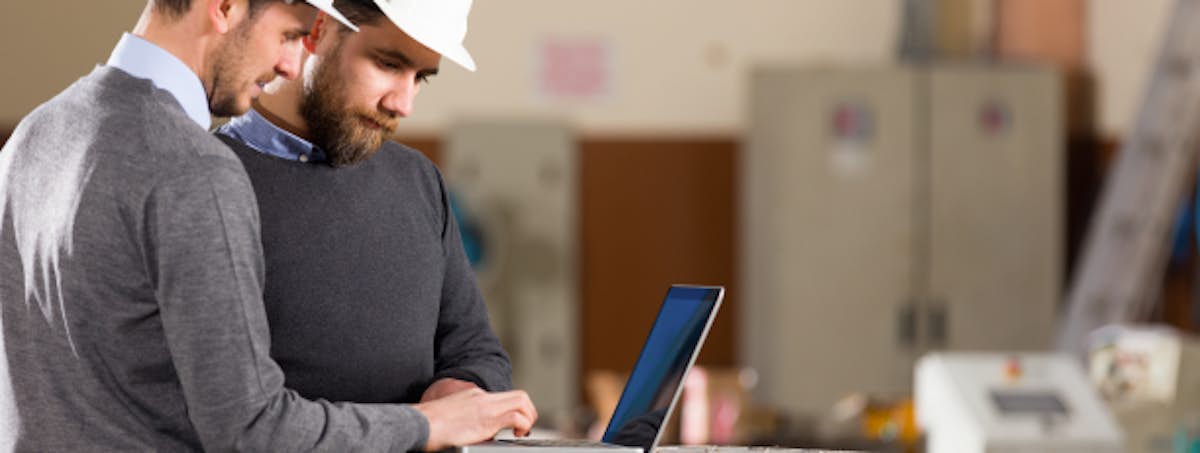 two men in hard hats looking at a laptop