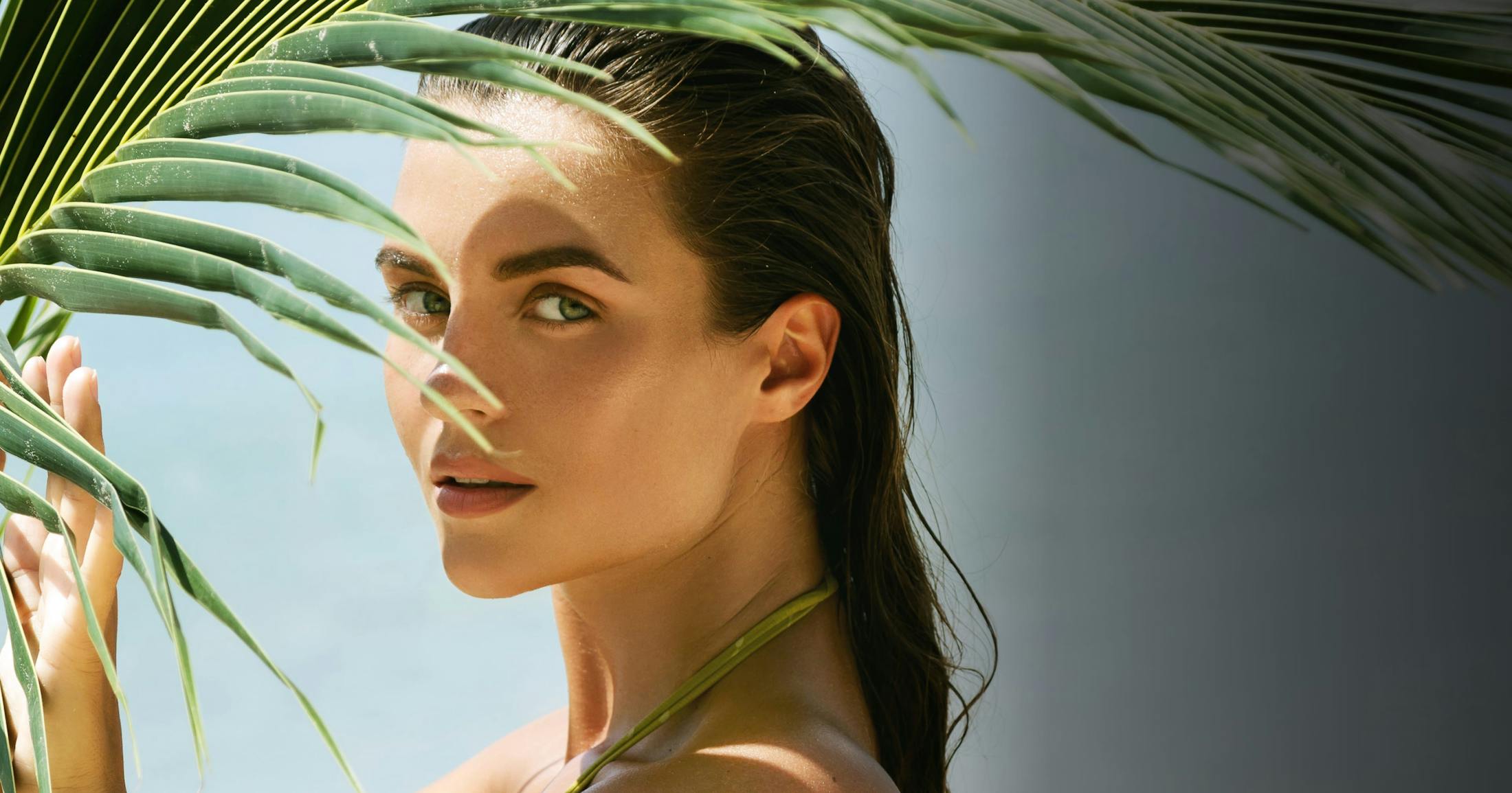 Woman that just got out of water standing by palm tree leaves