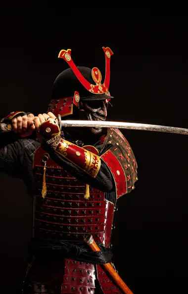 Samurai Armor A person dressed in traditional red samurai armor holds a katana with both hands, poised to strike, against a dark background.