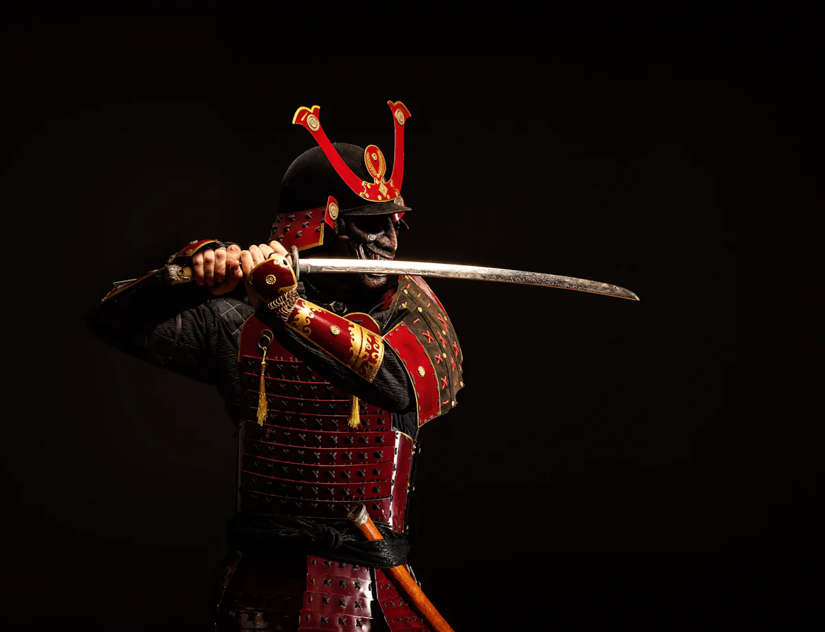Samurai Armor A person dressed in traditional red samurai armor holds a katana with both hands, poised to strike, against a dark background.