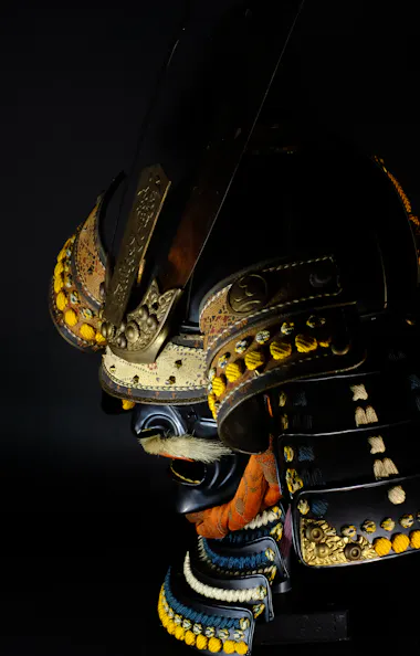 Samurai Armor A close-up of an ornate, traditional Japanese samurai helmet and armor with gold detailing, orange cords, and decorative patterns, set against a dark background.