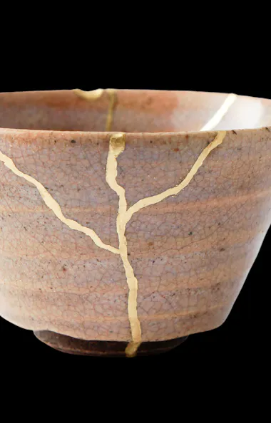 Kintsugi A ceramic bowl repaired with visible gold lines along its cracks, highlighting the Japanese art of kintsugi, set against a solid black background.