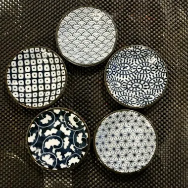 Kintsugi Workshop Five small round dishes with different blue and white geometric and floral patterns are arranged in a circle on a textured dark brown surface.