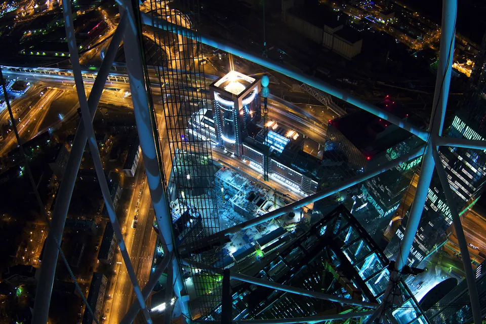 Tokyo Skytree at night A night aerial view of a city with a complex network of illuminated roads and highways. Skyscrapers and buildings are lit up, creating a vibrant cityscape. The image is framed by the structure of a tower or tall framework in the foreground.