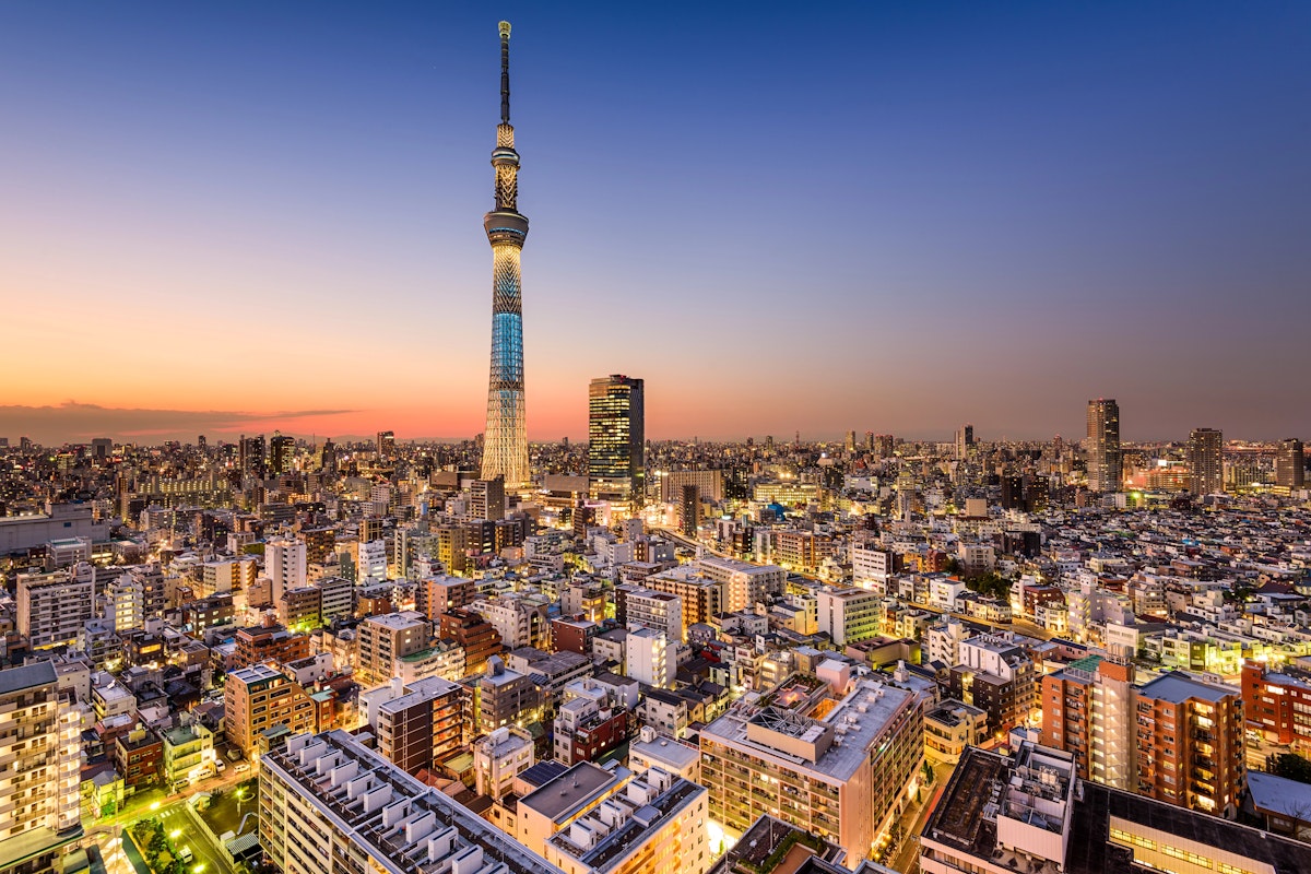 Tokyo Skytree A panoramic view of Tokyo at dusk featuring the illuminated Tokyo Skytree prominently in the center. The cityscape below is densely packed with buildings, and the sky transitions from a warm orange to a deep blue as evening sets in.