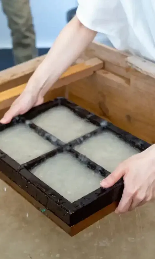 Washi Paper Making A person holds a wooden frame with four sections over a vat of water, demonstrating a traditional papermaking process.