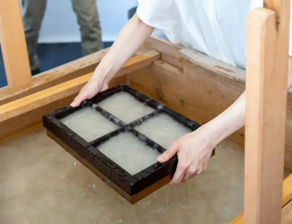 Washi Paper Making A person holds a wooden frame with four sections over a vat of water, demonstrating a traditional papermaking process.