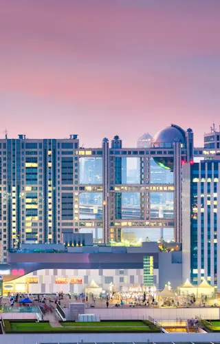 Odaiba Colorful cityscape of Tokyo at sunset, featuring modern high-rise buildings, the Rainbow Bridge, and Tokyo Tower in the background under a pink and purple sky.