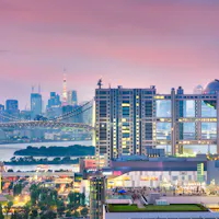 Odaiba Colorful cityscape of Tokyo at sunset, featuring modern high-rise buildings, the Rainbow Bridge, and Tokyo Tower in the background under a pink and purple sky.