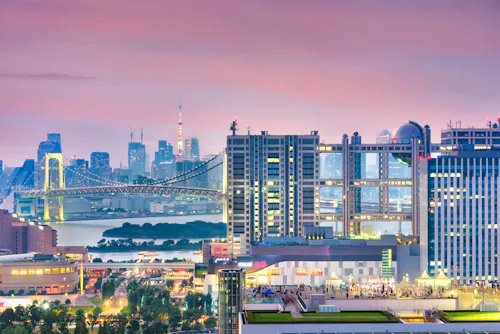 Colorful cityscape of Tokyo at sunset, featuring modern high-rise buildings, the Rainbow Bridge, and Tokyo Tower in the background under a pink and purple sky.