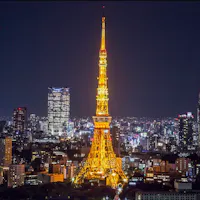Tokyo Tower A night view of a city with a brightly illuminated tower in the center, resembling Tokyo Tower. Surrounding the tower are numerous buildings with scattered lights, creating a vibrant cityscape against a dark sky.