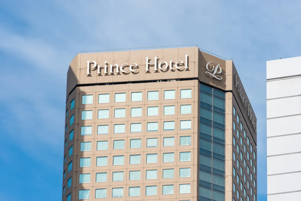 Shinagawa Prince Hotel A tall, tan building with white-framed windows and the text "Prince Hotel" displayed near the top. The logo "P" is also visible beside the text. The sky is clear and blue, providing a backdrop to the building.