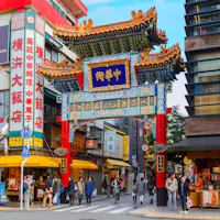 Yokohama's Chinatown Street scene in Yokohama Chinatown, featuring a colorful traditional Chinese gate with intricate designs. People walk and shop at various stores, including restaurants and souvenir shops. Bright signs with Chinese characters are prominently displayed on the buildings.