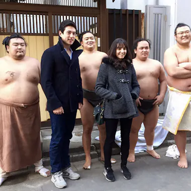 Sumo Wrestlers A group of five men, four in sumo attire and one in a coat, stand outdoors next to a woman in a gray jacket. The sumo wrestlers are barefoot; the group poses and smiles for the photo on a sidewalk.
