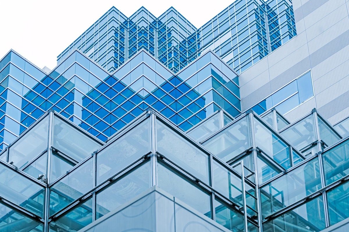 Historic and Contemporary Architecture A modern building with a glass facade and a geometric design, featuring overlapping layers of reflective blue glass panels. The structure showcases a blend of angles and lines, creating a dynamic and intricate architectural pattern against the sky.