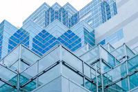 A modern building with a glass facade and a geometric design, featuring overlapping layers of reflective blue glass panels. The structure showcases a blend of angles and lines, creating a dynamic and intricate architectural pattern against the sky.