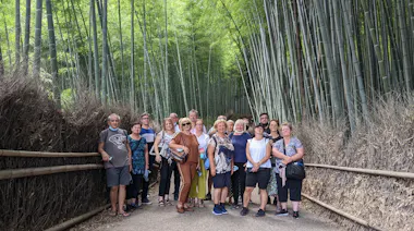 A group of people pose together on a path surrounded by tall bamboo trees, with wooden railings and dense greenery in the background.