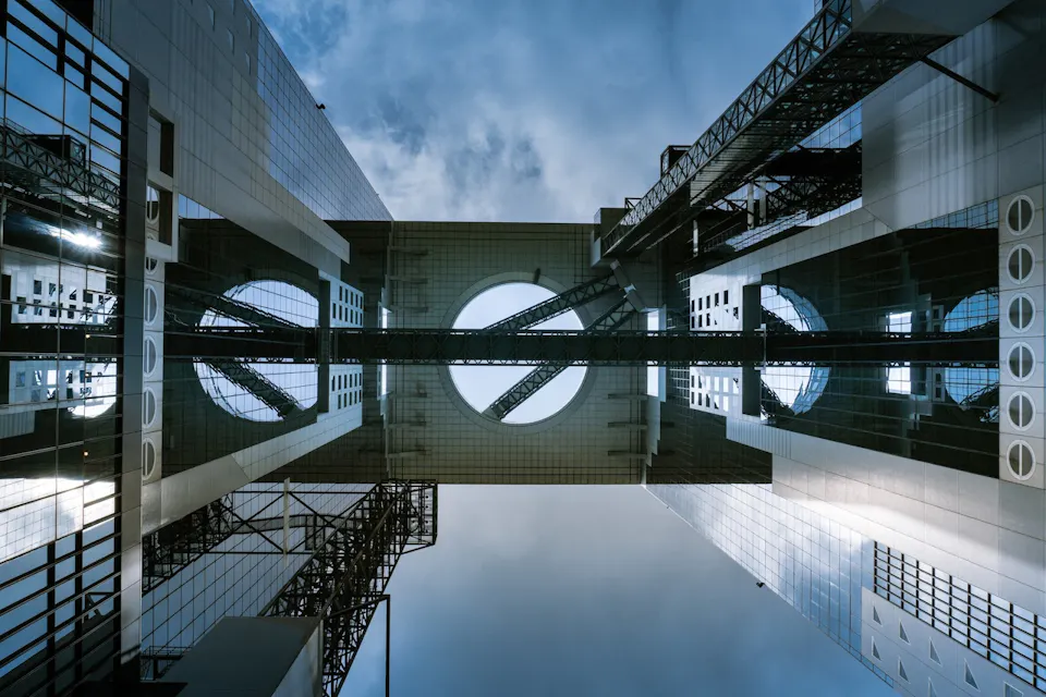 Umeda Sky Building 从低角度看现代建筑,展示了两个高高并行的结构,通过带有圆形开口的高架连接。天空通过开口可见,建筑的玻璃表面上可见反射。