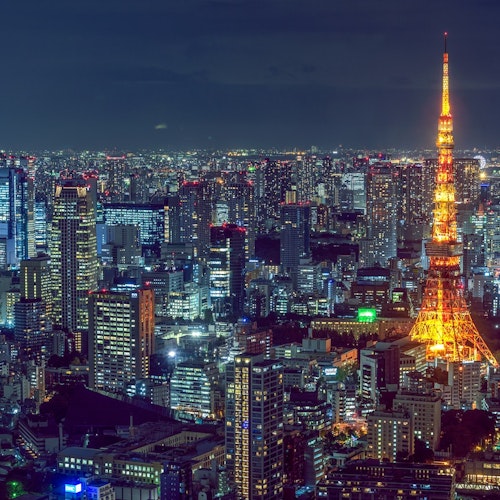 Tokyo at Night A nighttime aerial view of Tokyo, Japan, featuring a vibrant cityscape illuminated by numerous lights. The brightly lit Tokyo Tower stands prominently in the center, glowing with a warm orange hue against the backdrop of dark buildings and the night sky.