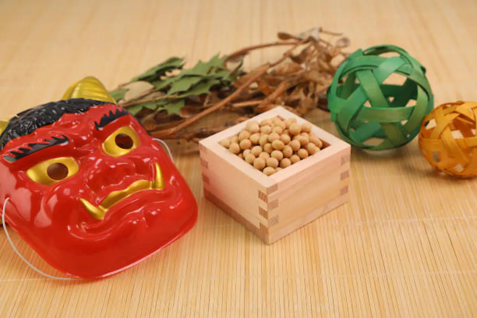 Setsubun A red oni mask beside a wooden box of roasted soybeans and a holly sprig