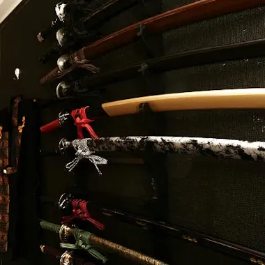 Samurai Swords A collection of Japanese swords with ornate handles and scabbards is displayed on a wall-mounted rack, some with decorative wrappings and unique patterns.