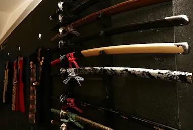 A collection of Japanese swords with ornate handles and scabbards is displayed on a wall-mounted rack, some with decorative wrappings and unique patterns.
