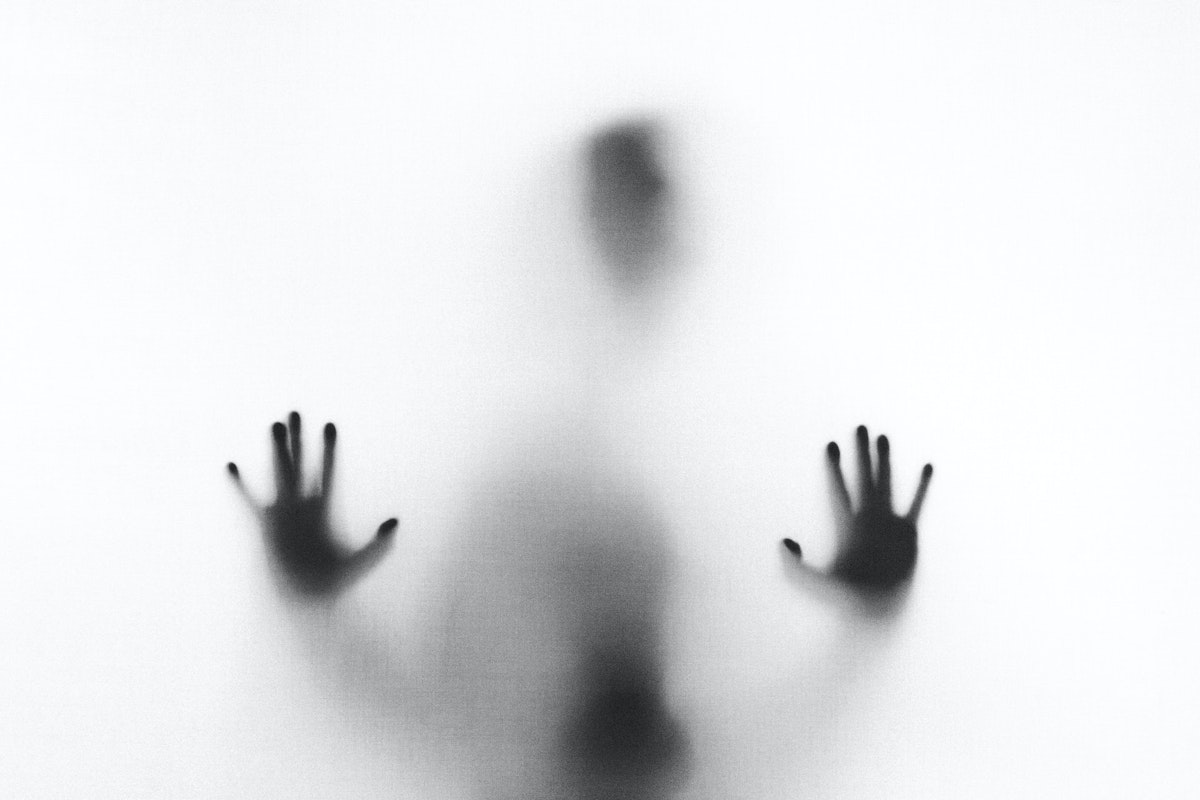 Paranormal Image A blurry silhouette of a person with their hands pressed against a frosted or opaque surface. The image captures an ambiguous and mysterious figure, with the details of the face and body obscured.