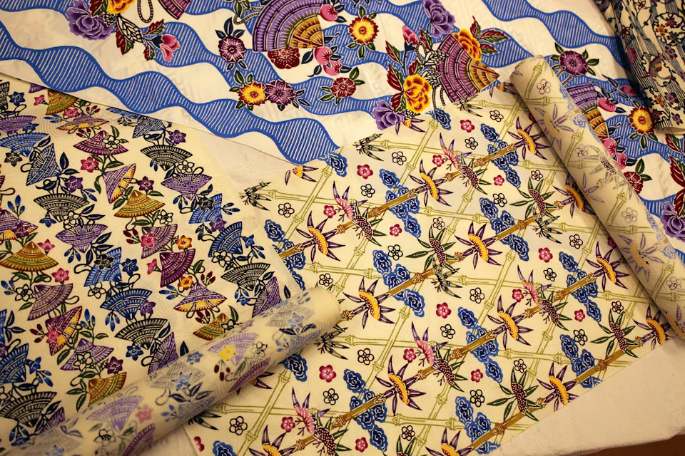 Bingata Textiles 五颜六色的图案织物卷展示着生动的花卉、几何和抽象设计,色彩调色板包括紫色、蓝色、黄色和绿色。织物图案包括花朵、星星和条纹波浪等元素。