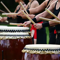 Sado's Taiko Traditions A group of people dressed in black tank tops and red sashes play traditional Japanese taiko drums. They are positioned in a row, striking the drums with thick wooden sticks, their arms raised mid-movement. The drums are large and feature decorative rope bindings.